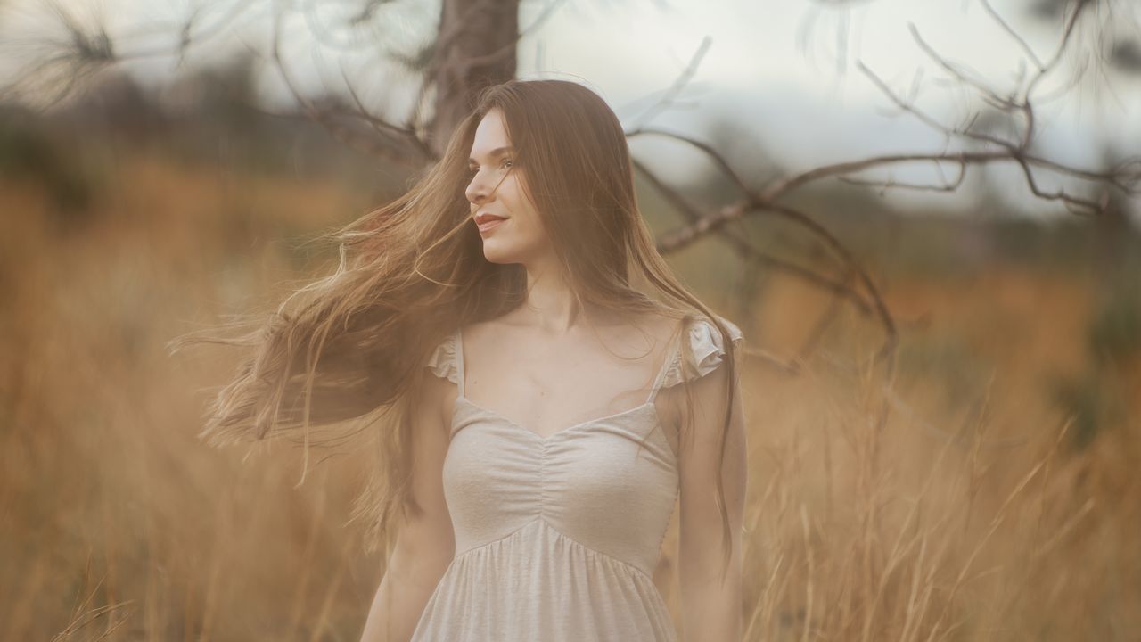 About Elegant woman with flowing hair in a tranquil rural field, evoking a serene and natural atmosphere.