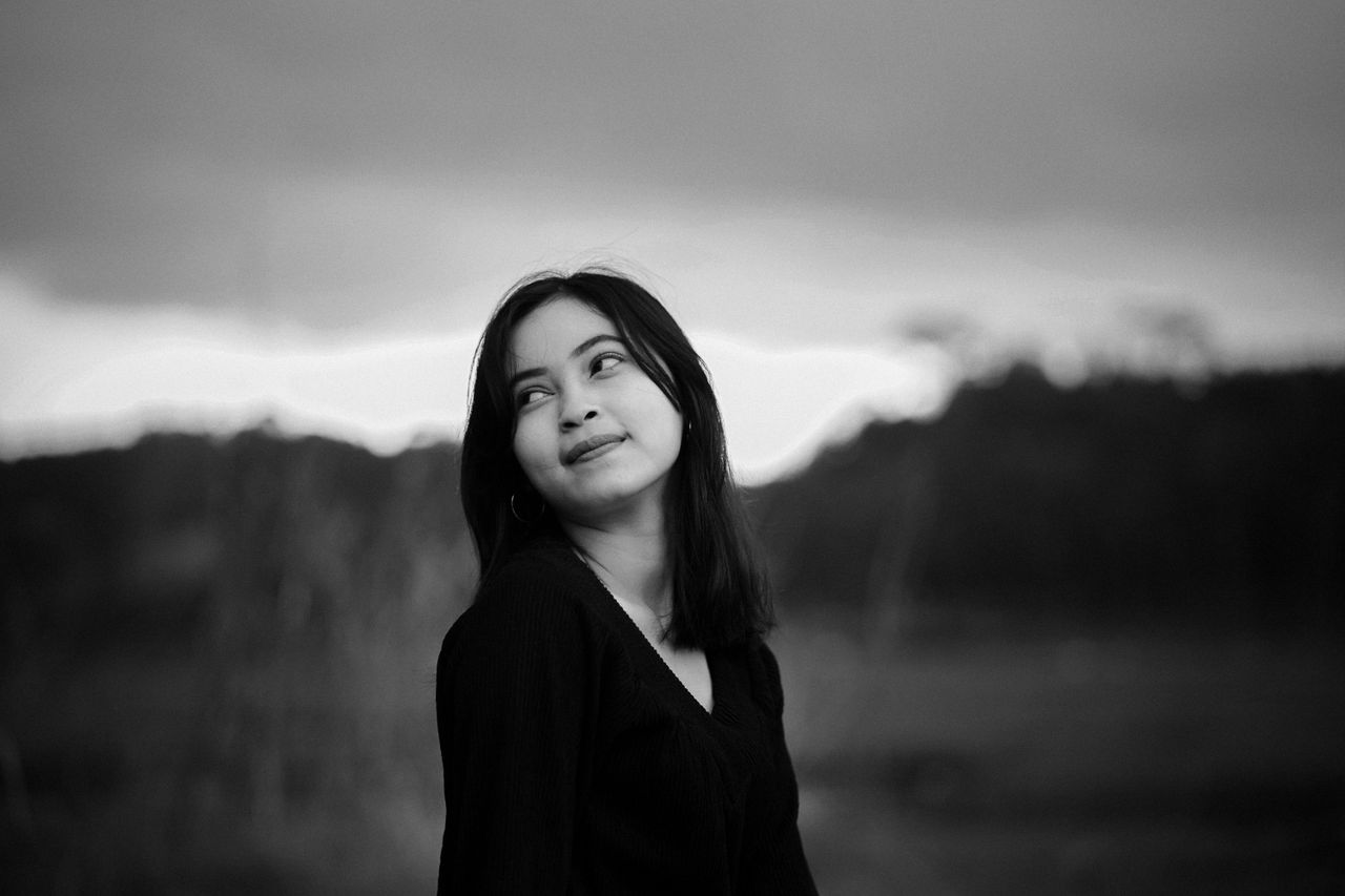 Services A captivating black and white portrait of a young woman looking upwards outdoors.